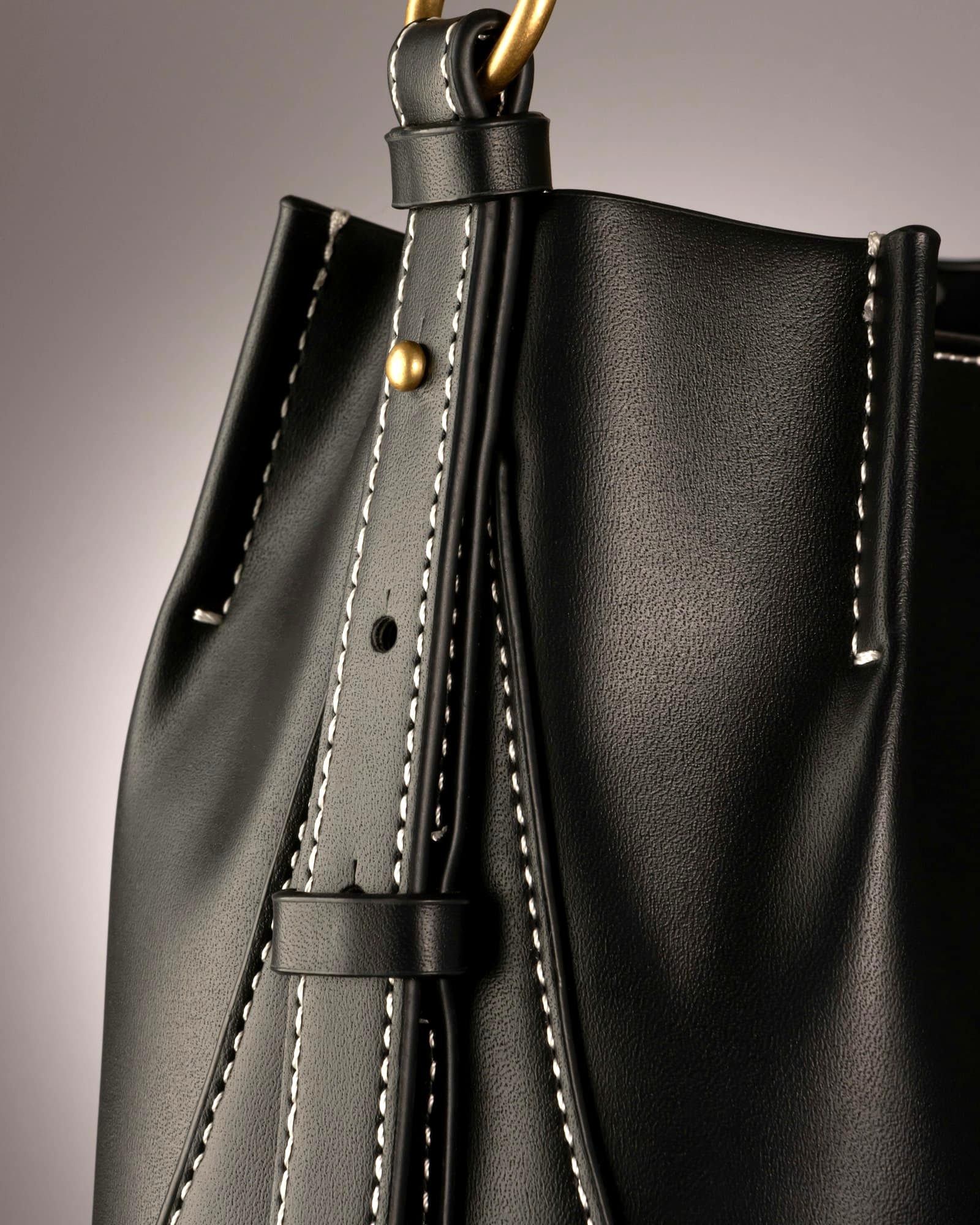 Black leather bucket bag with contrast saddle stitching, grey background