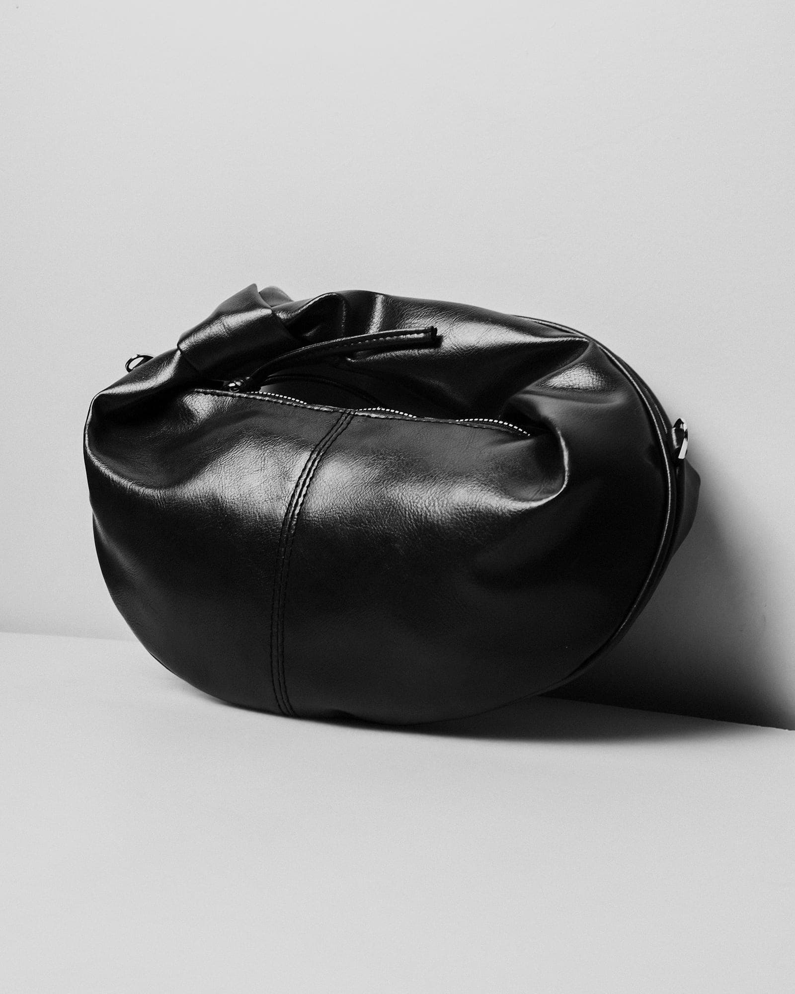 Soft black leather hobo bag slouched against a white wall