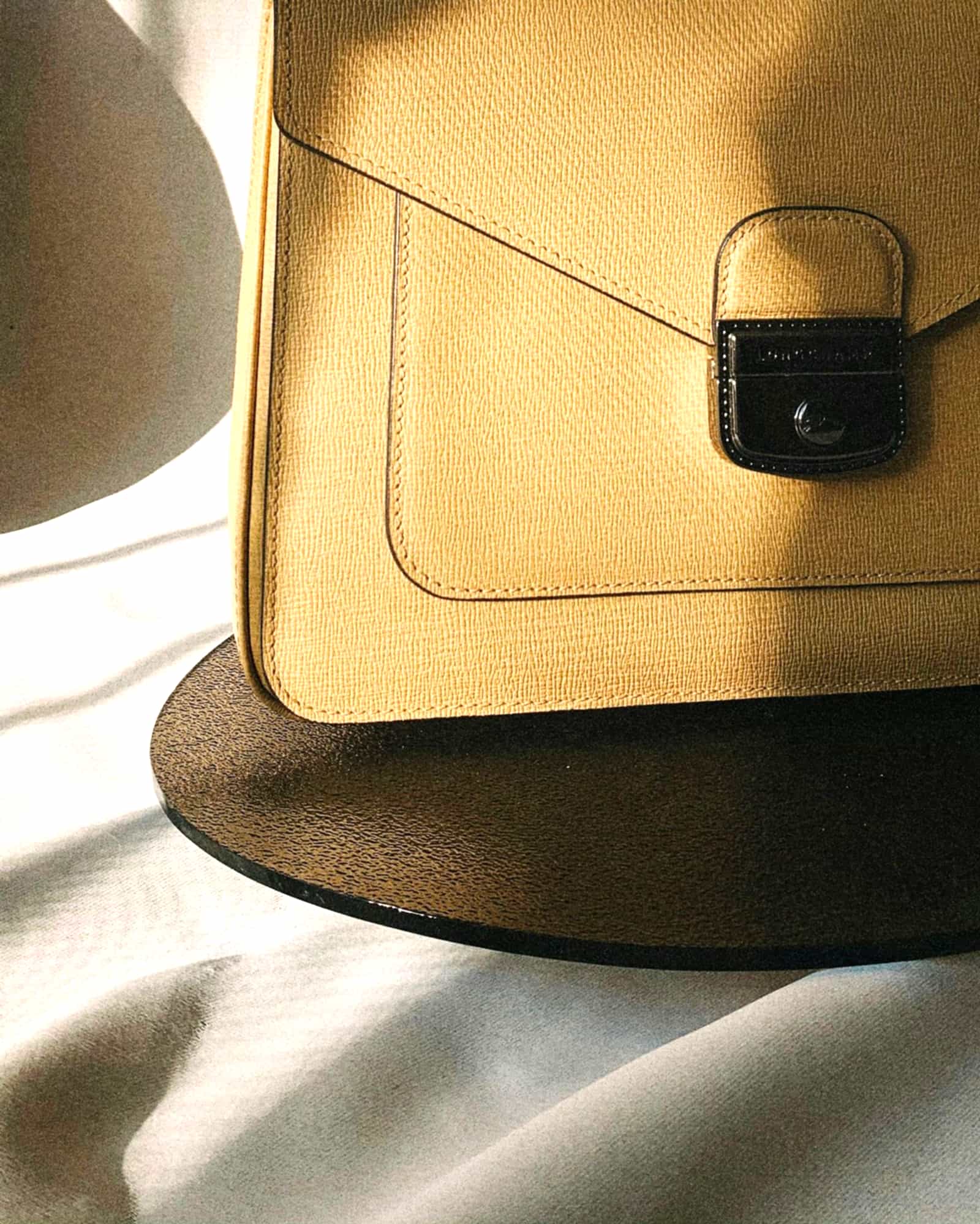 Tan textured envelope bag with a flap lock, raking window light