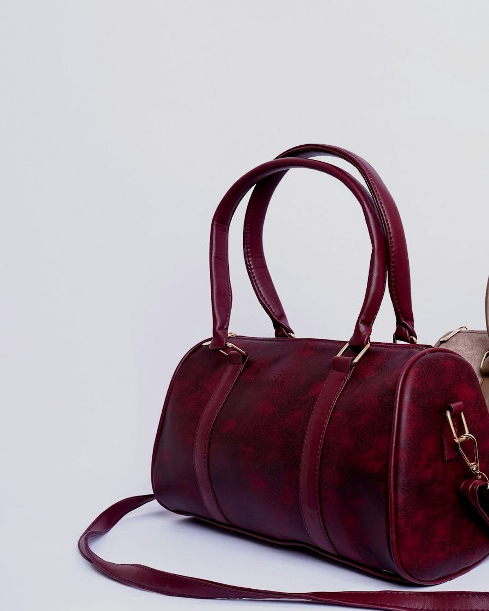 Small burgundy leather barrel bag with a shoulder strap, white background