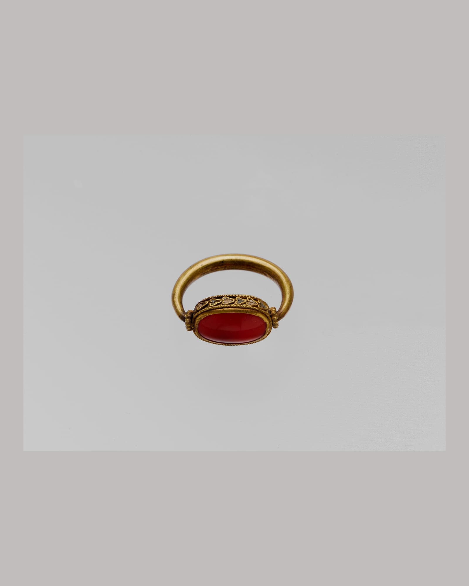 Yellow-gold signet ring with a carved carnelian stone, grey background
