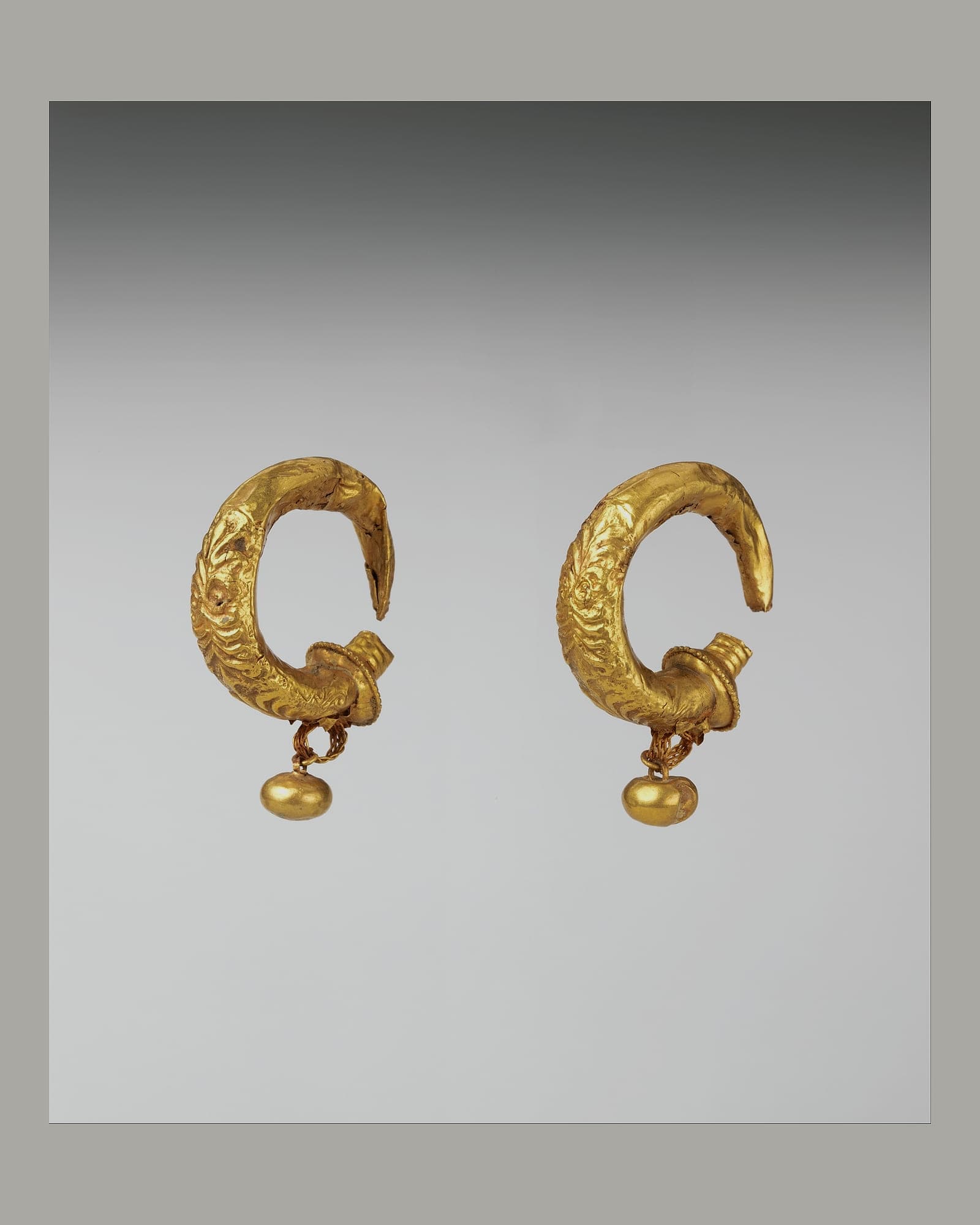 Pair of sculpted yellow-gold hoop earrings, grey background