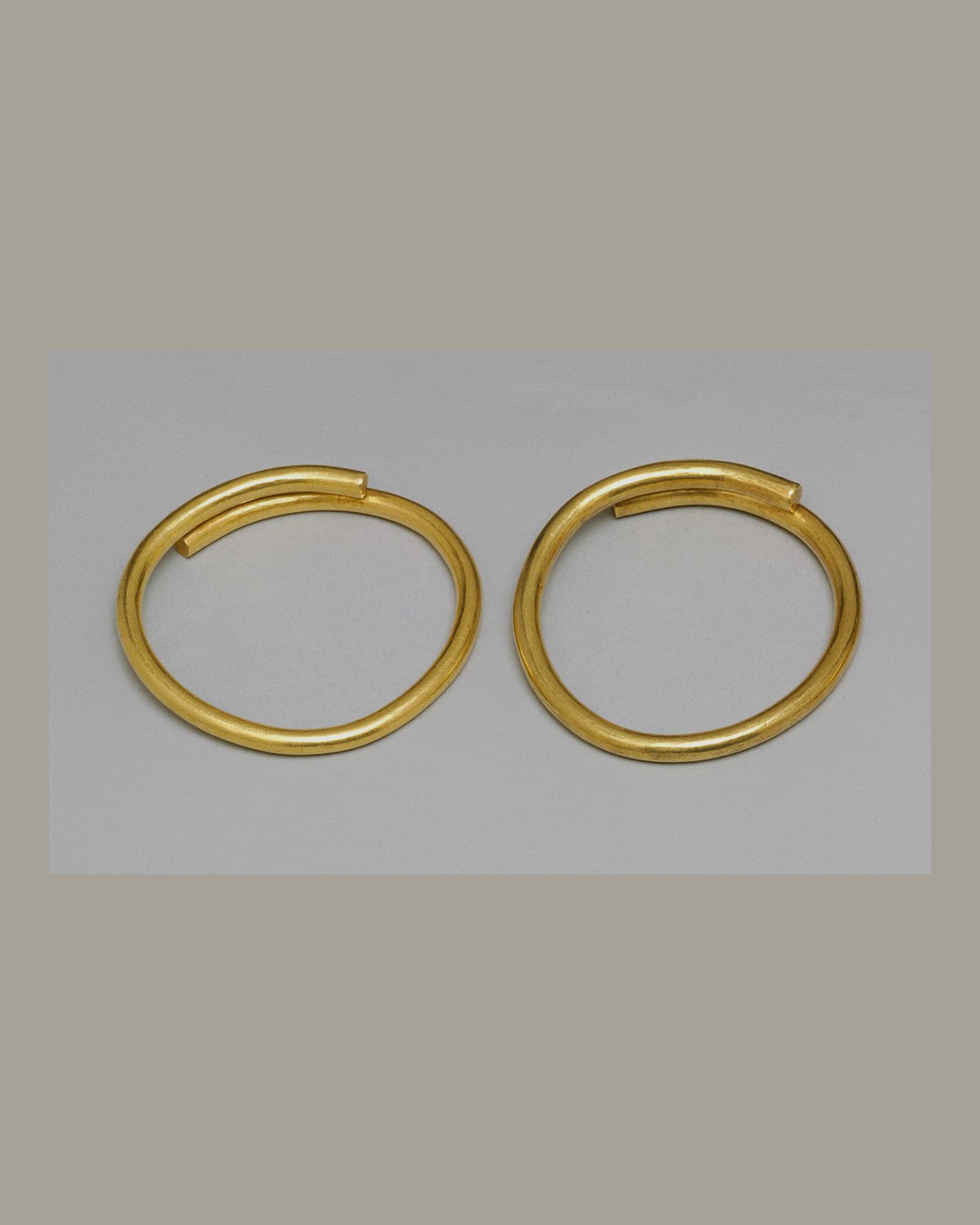 Pair of plain yellow-gold bangles, pale grey background