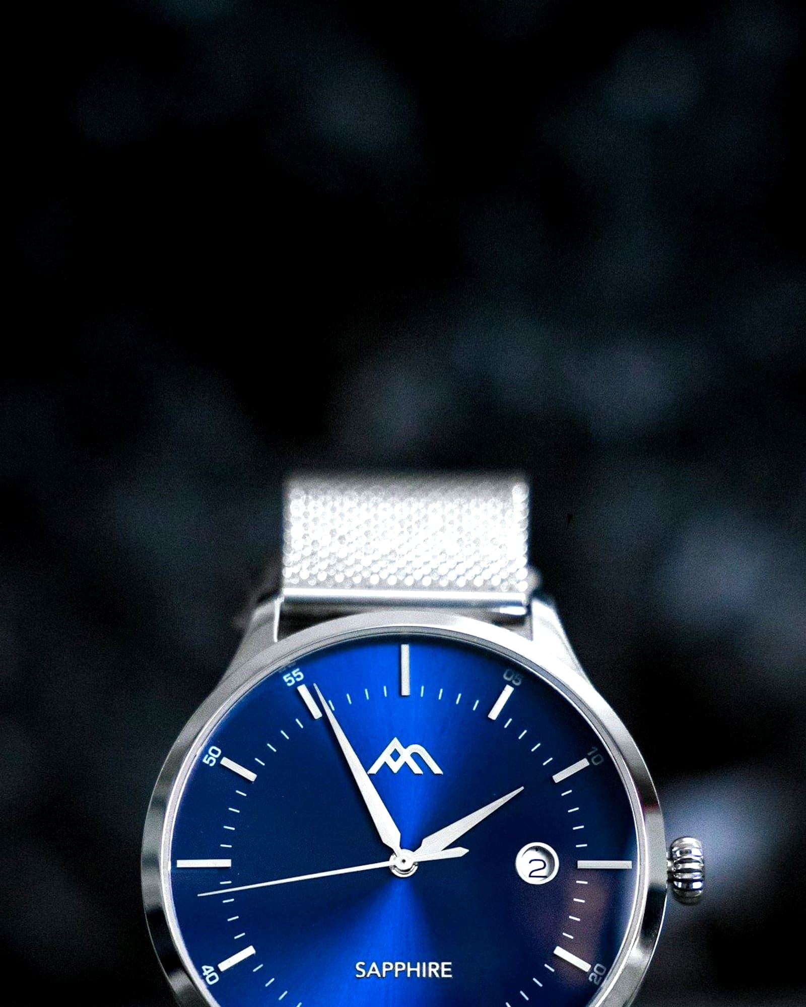 Steel watch with a sunburst blue dial on a woven mesh bracelet — detail view