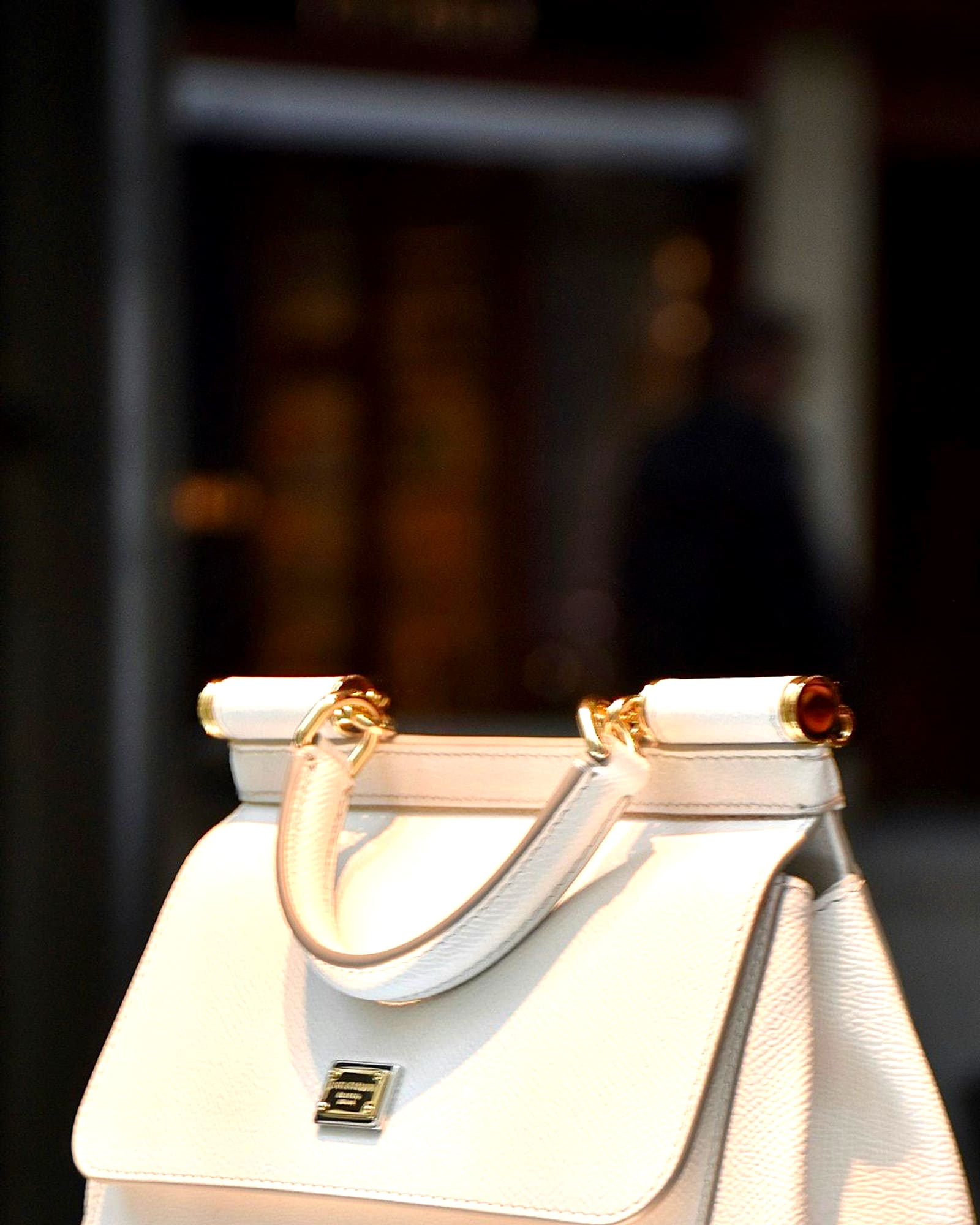 Cream leather top-handle bag with gold clasp, softly blurred background — detail view
