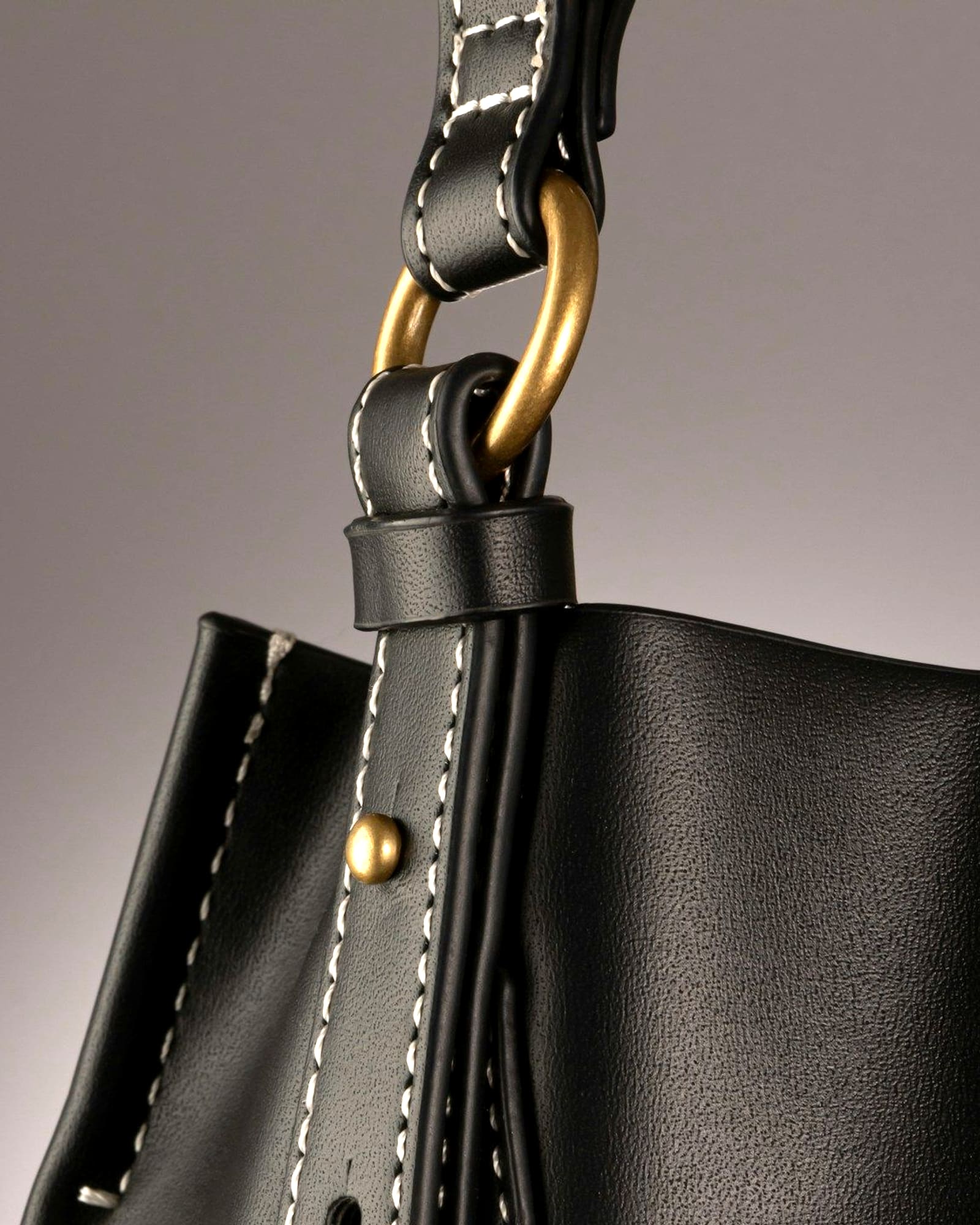 Black leather bucket bag with contrast saddle stitching, grey background — detail view