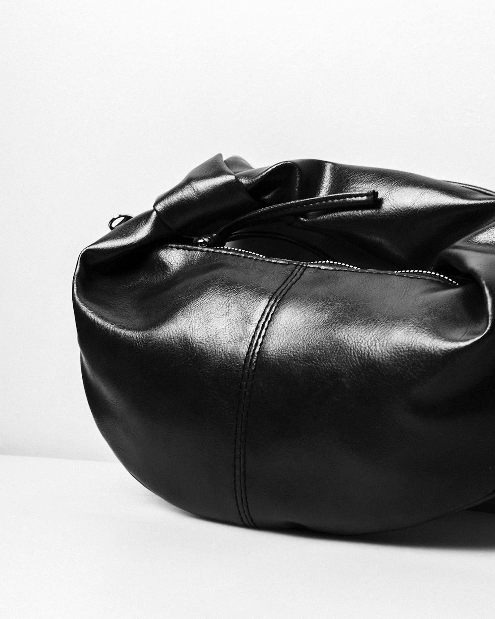 Soft black leather hobo bag slouched against a white wall — detail view