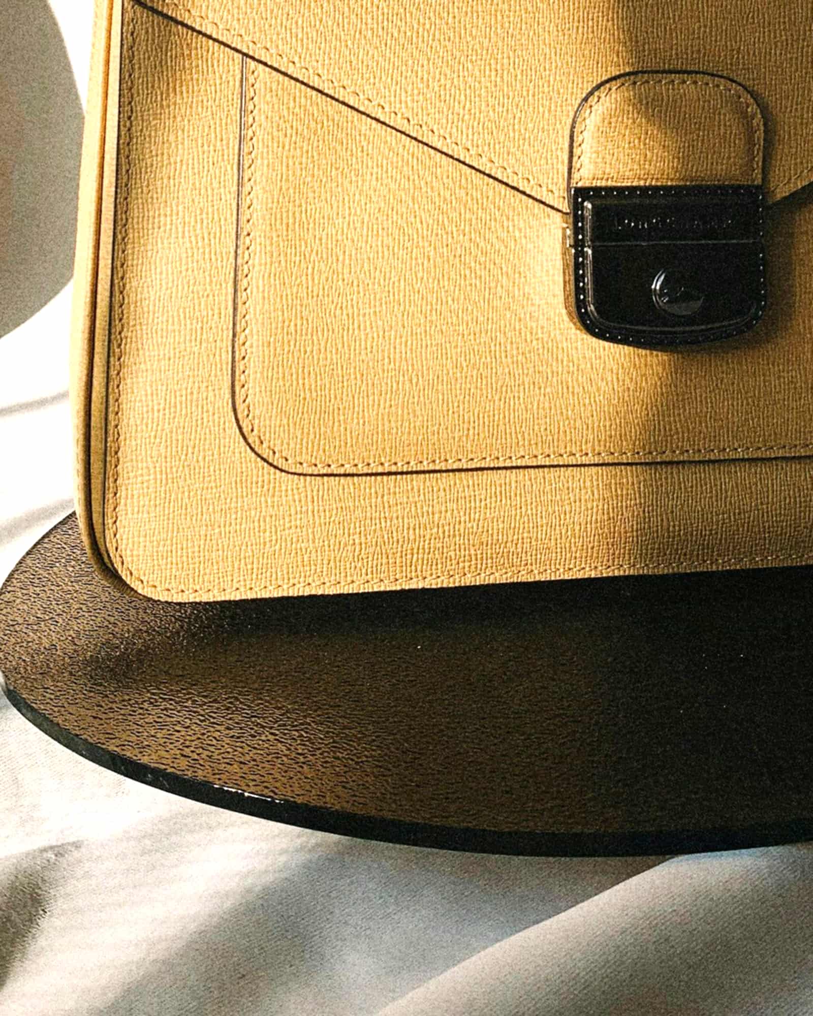 Tan textured envelope bag with a flap lock, raking window light — detail view