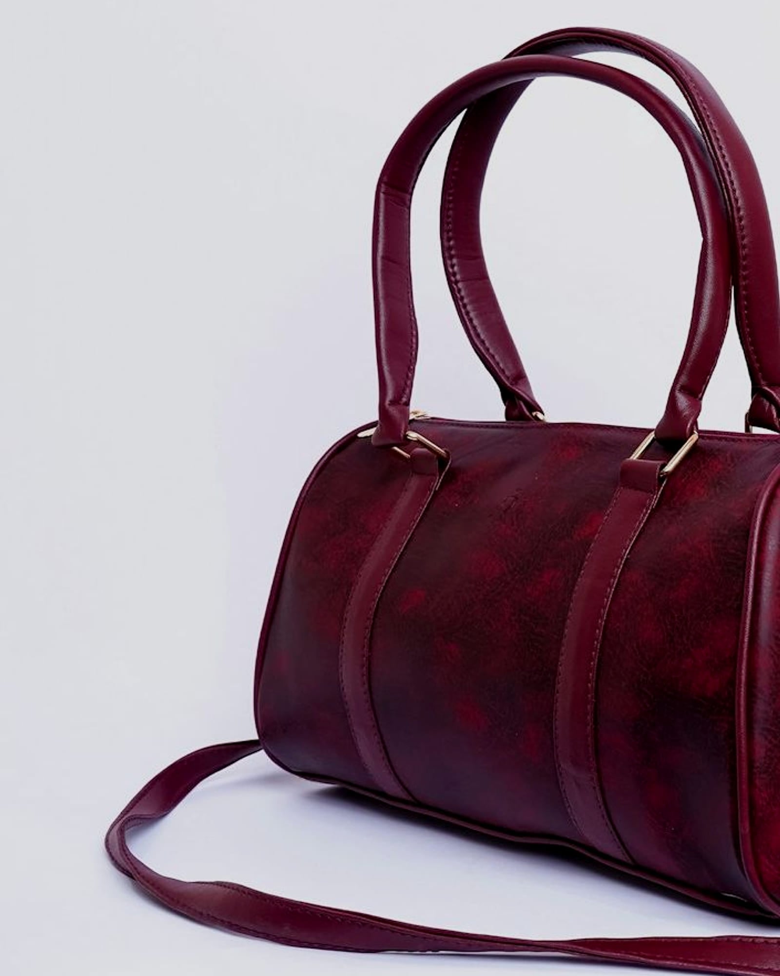 Small burgundy leather barrel bag with a shoulder strap, white background — detail view