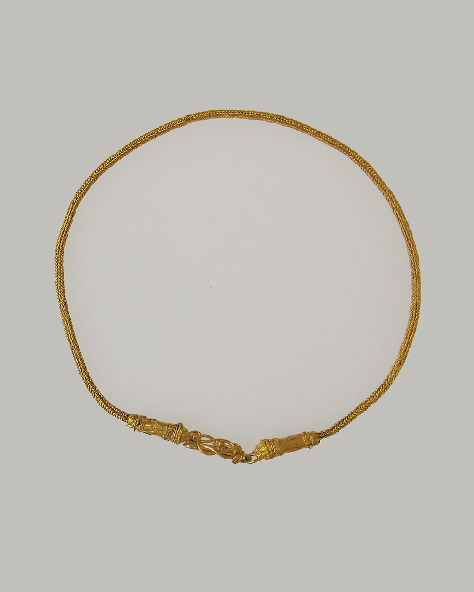 Slender yellow-gold collar necklace on a cream background — detail view