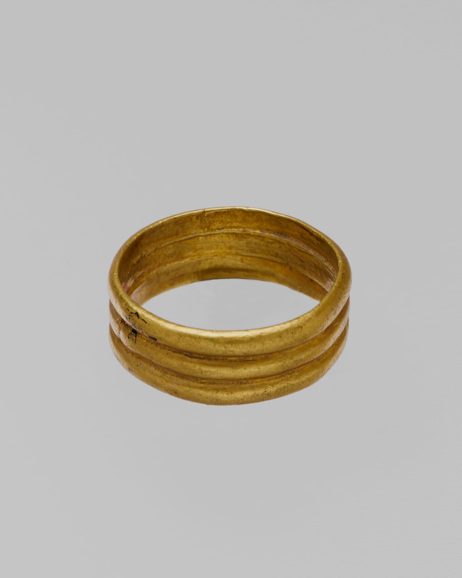 Plain yellow-gold band ring on a pale grey background — detail view