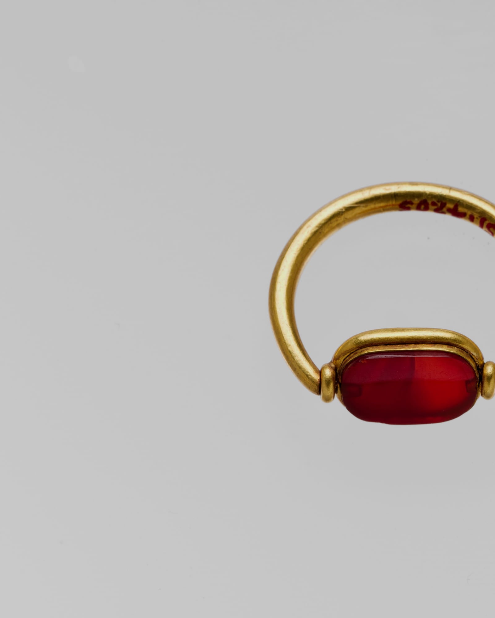 Yellow-gold ring set with a deep red cabochon, pale grey background — detail view