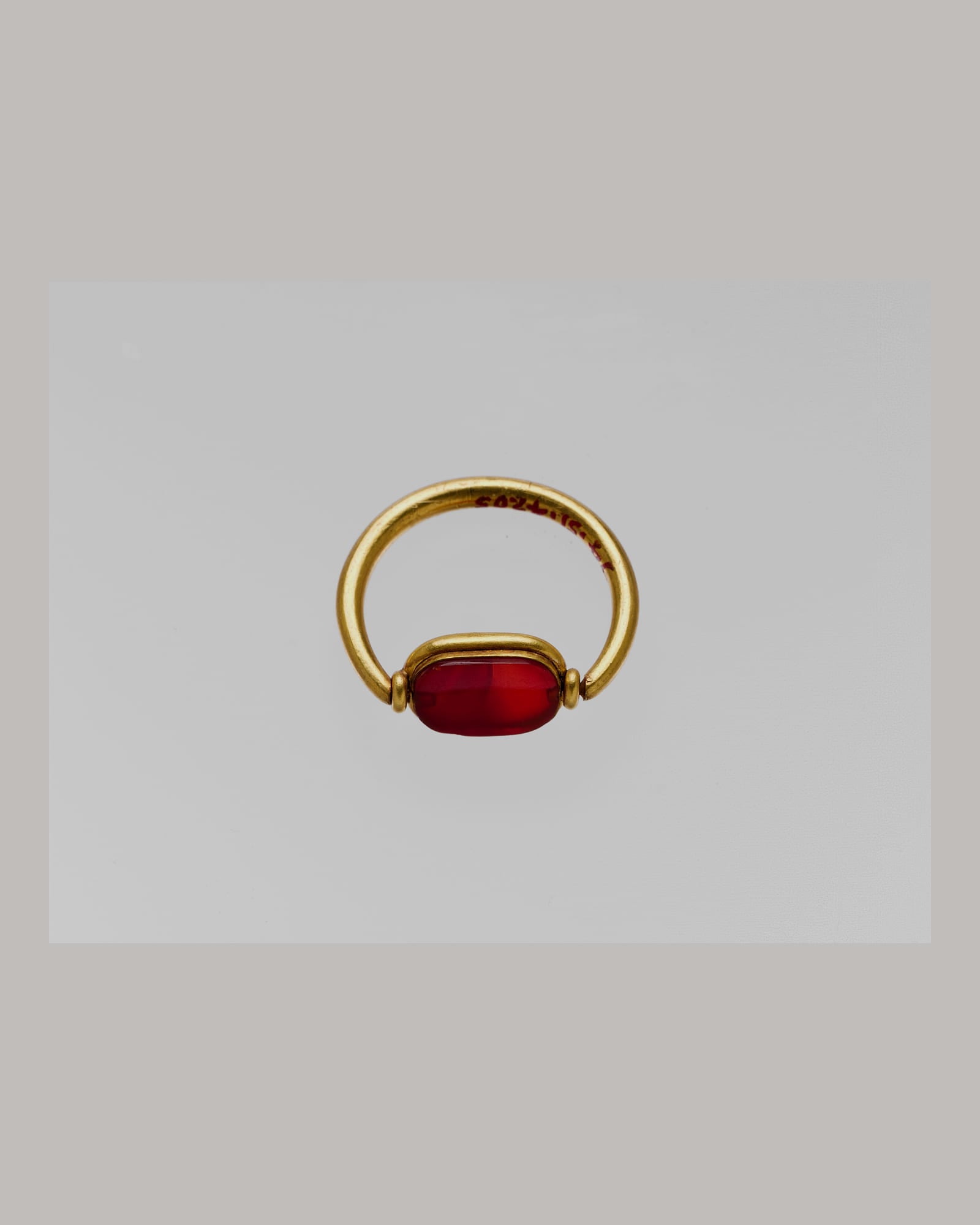 Yellow-gold ring set with a deep red cabochon, pale grey background