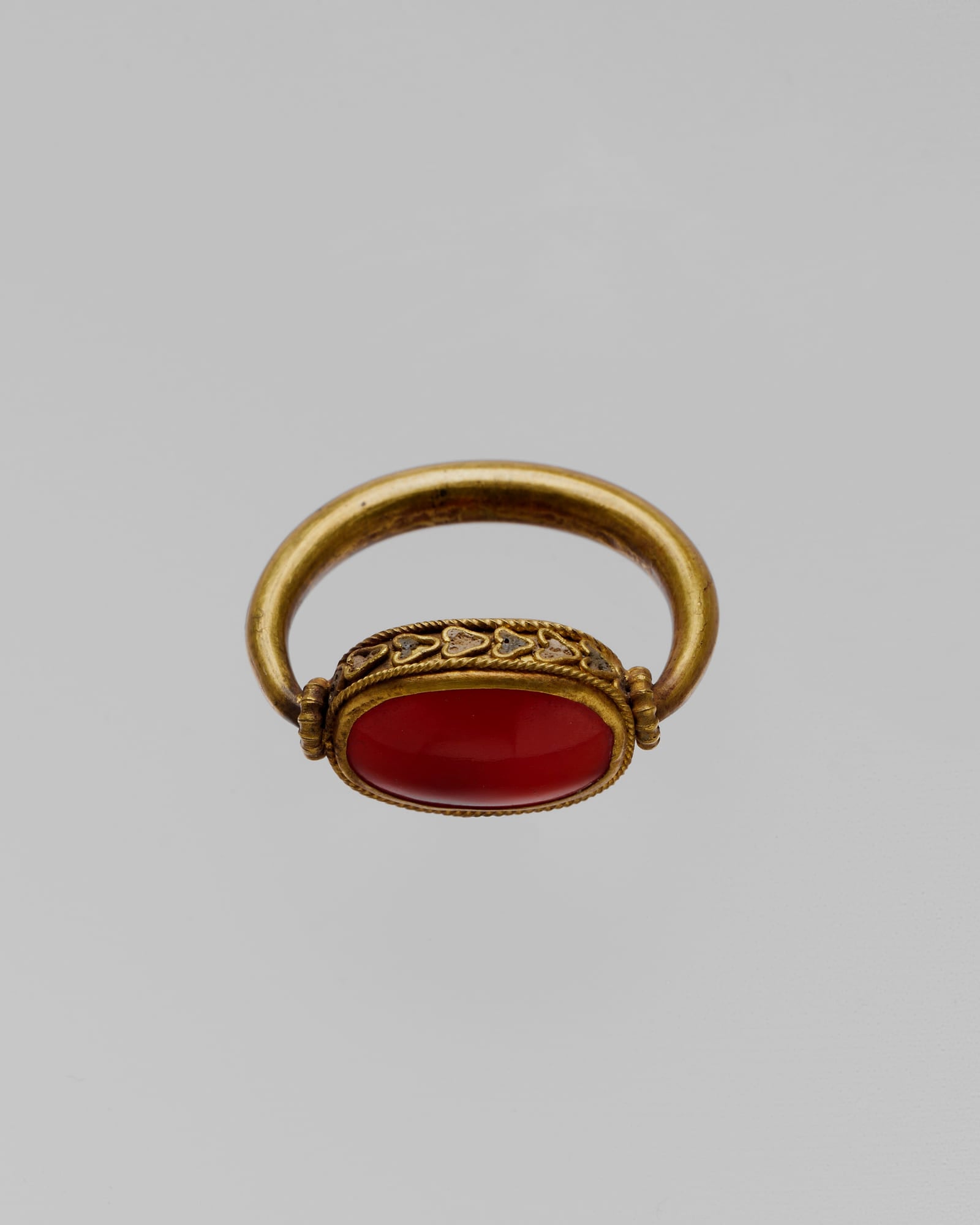 Yellow-gold signet ring with a carved carnelian stone, grey background — detail view