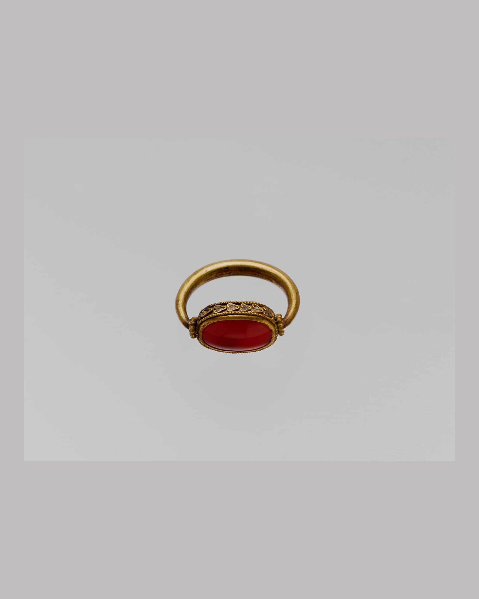 Yellow-gold signet ring with a carved carnelian stone, grey background