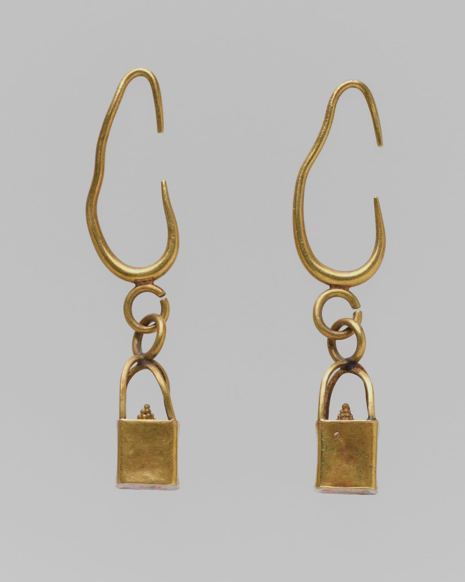 Pair of fine yellow-gold drop earrings, pale grey background — detail view