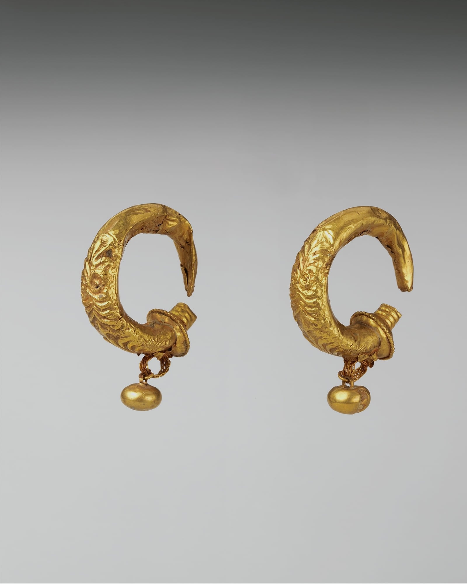 Pair of sculpted yellow-gold hoop earrings, grey background — detail view