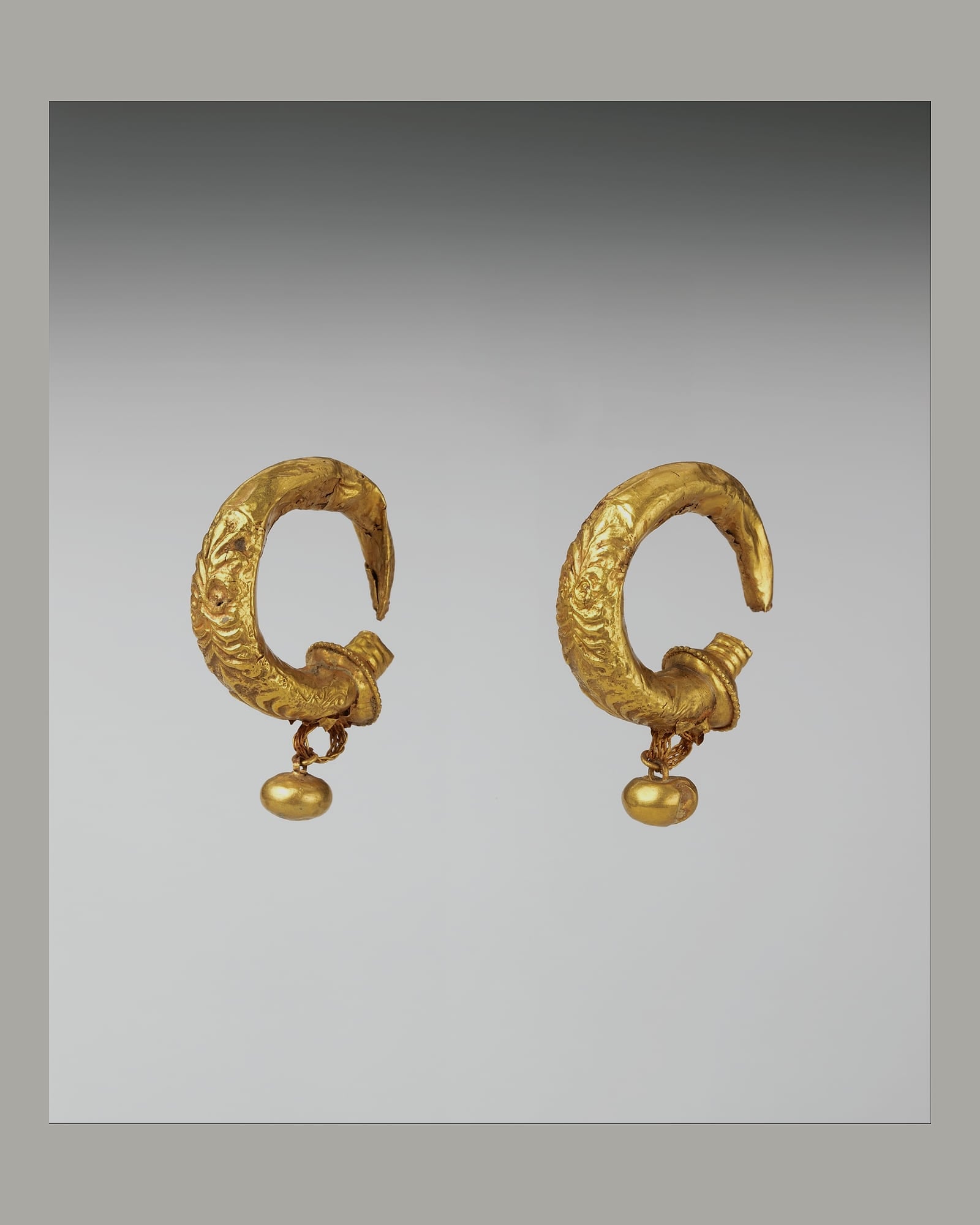 Pair of sculpted yellow-gold hoop earrings, grey background
