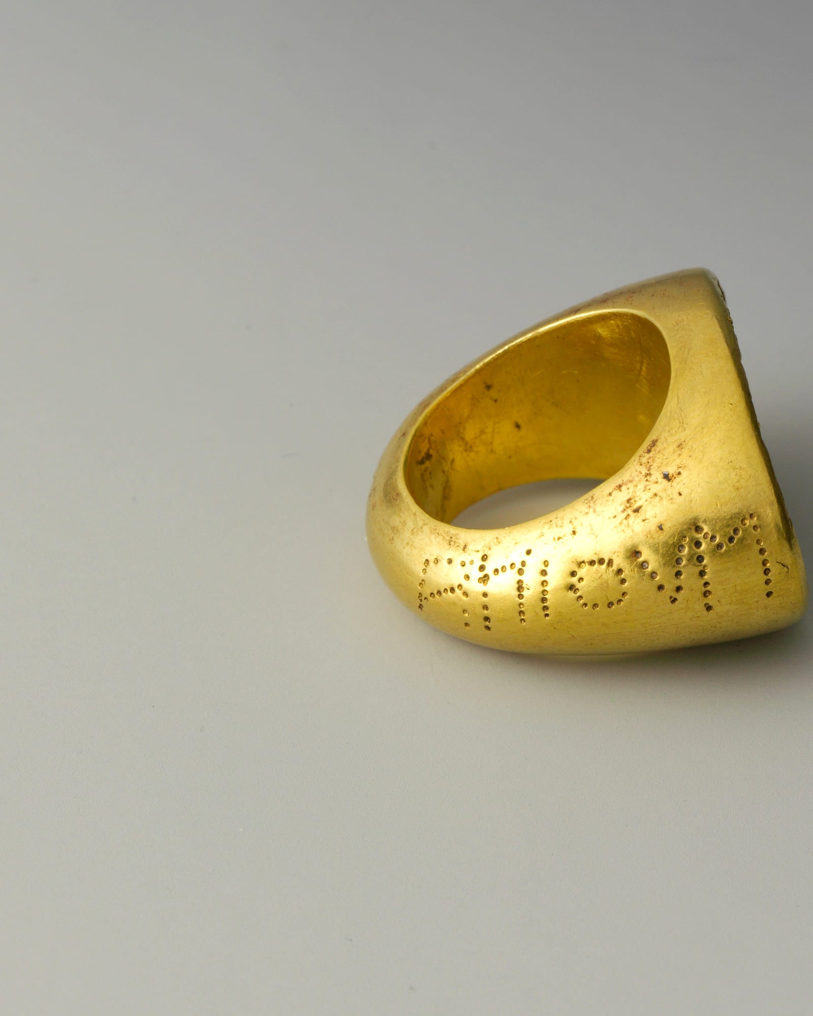 Heavy yellow-gold signet ring on a grey background — detail view
