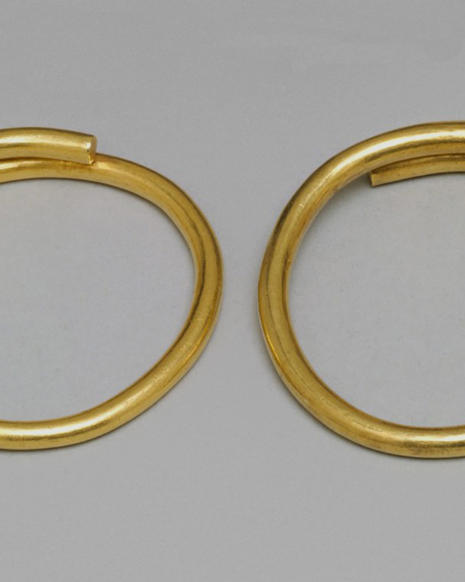 Pair of plain yellow-gold bangles, pale grey background — detail view