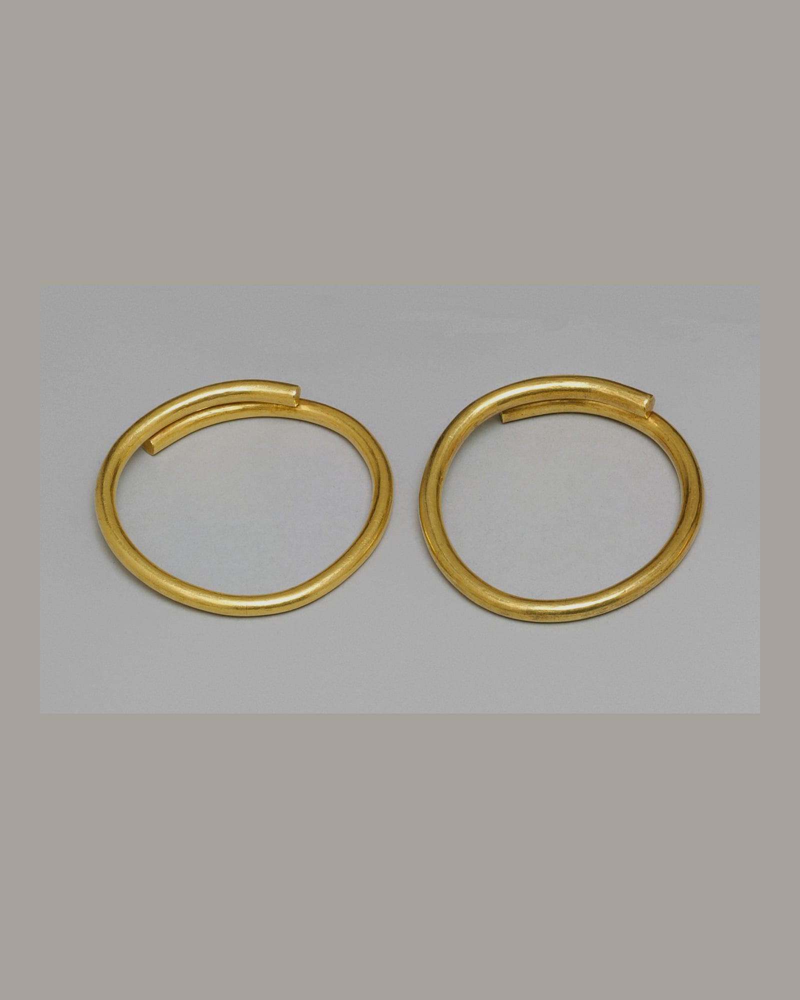Pair of plain yellow-gold bangles, pale grey background