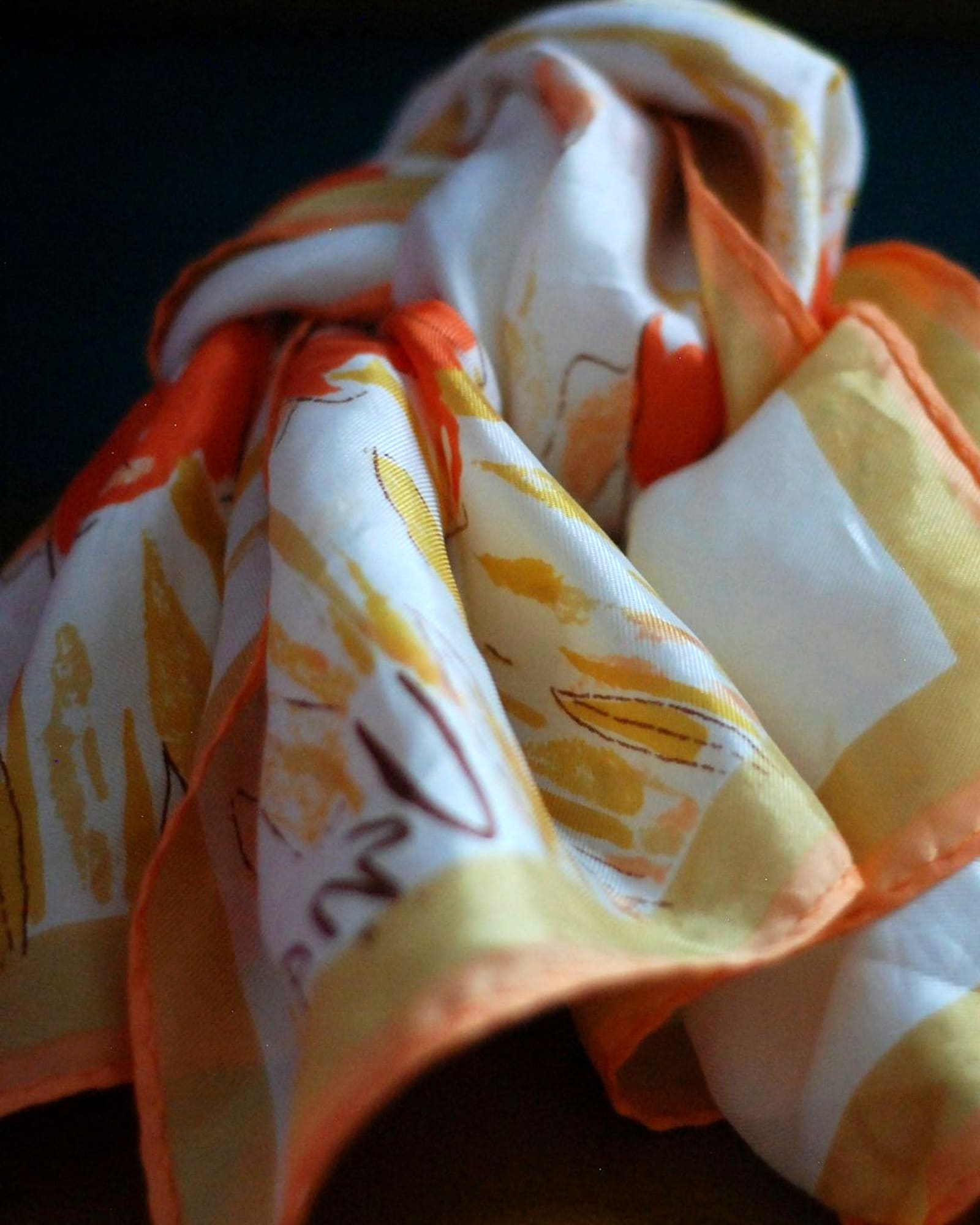 Ivory silk scarf with a coral border, loosely knotted — detail view