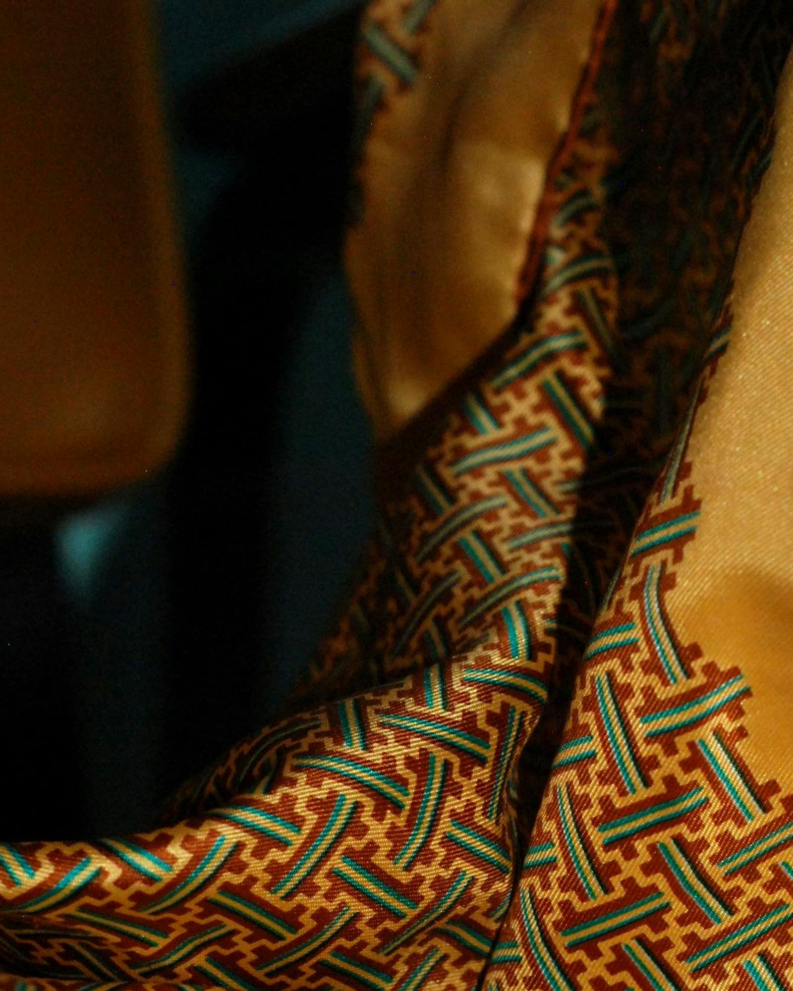 Ochre silk scarf with a green geometric border, folded across a chair — detail view