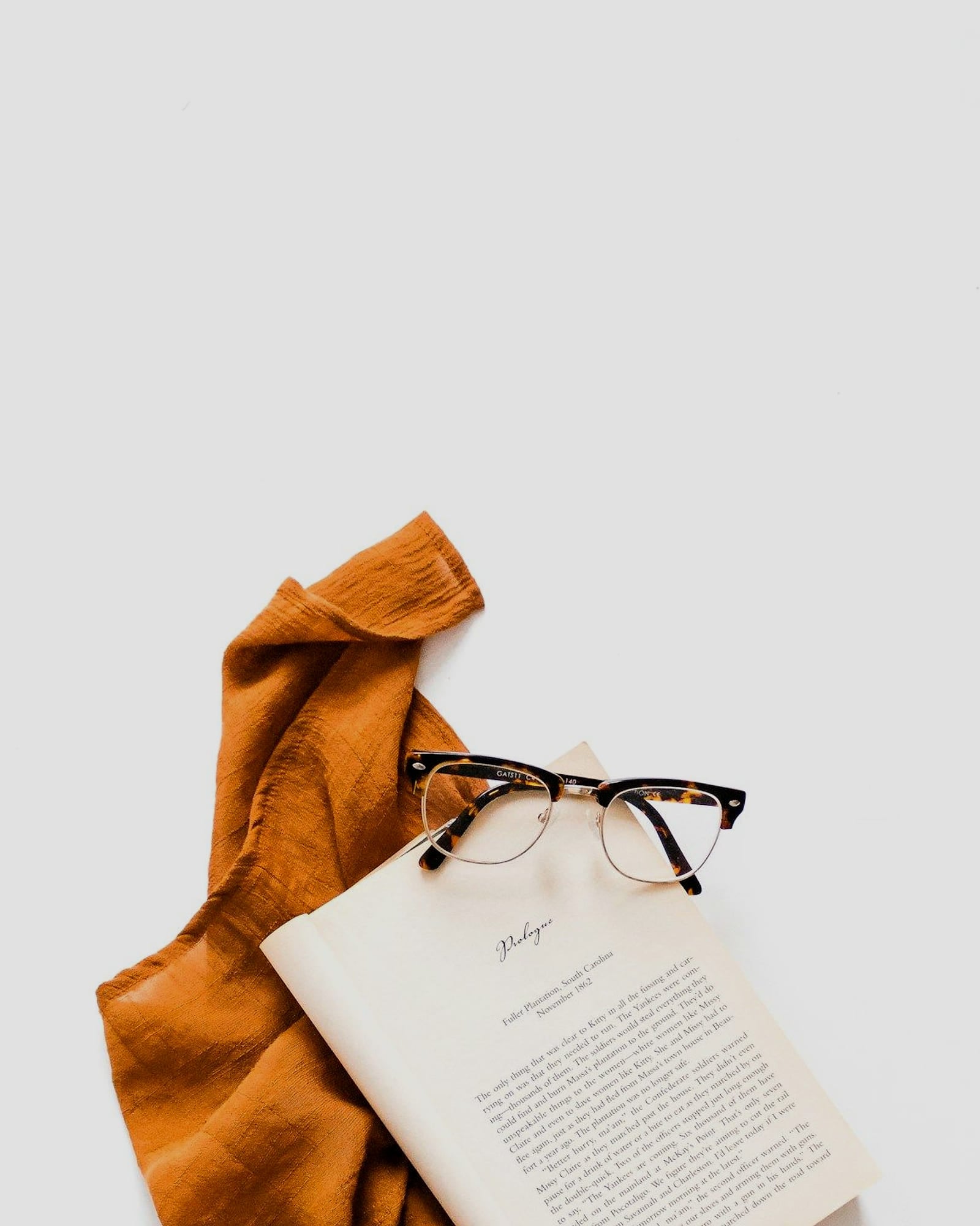 Rust-coloured scarf pooled on a white surface beside an open book — detail view