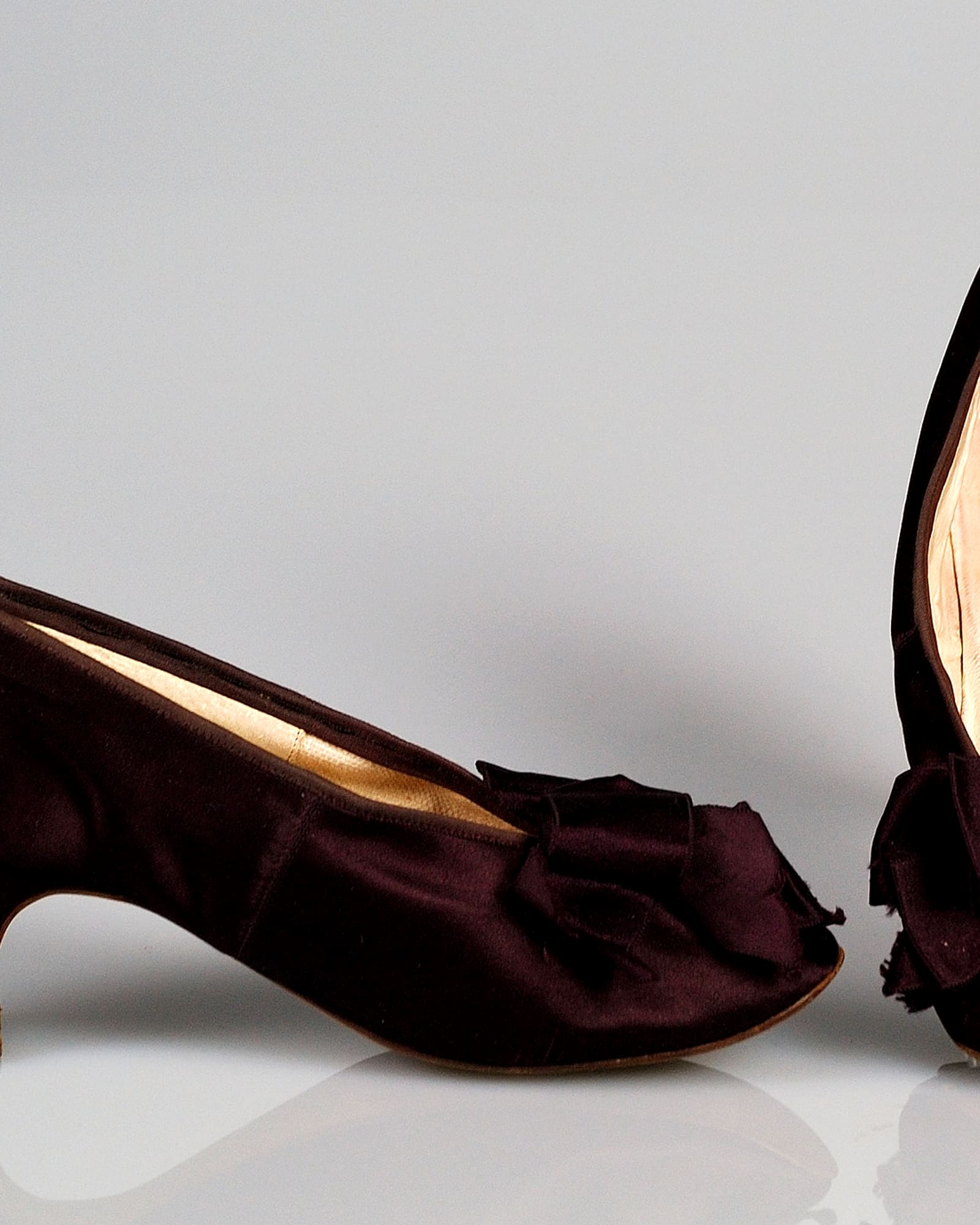 Pair of burgundy silk heels with ribbon bows, grey background — detail view