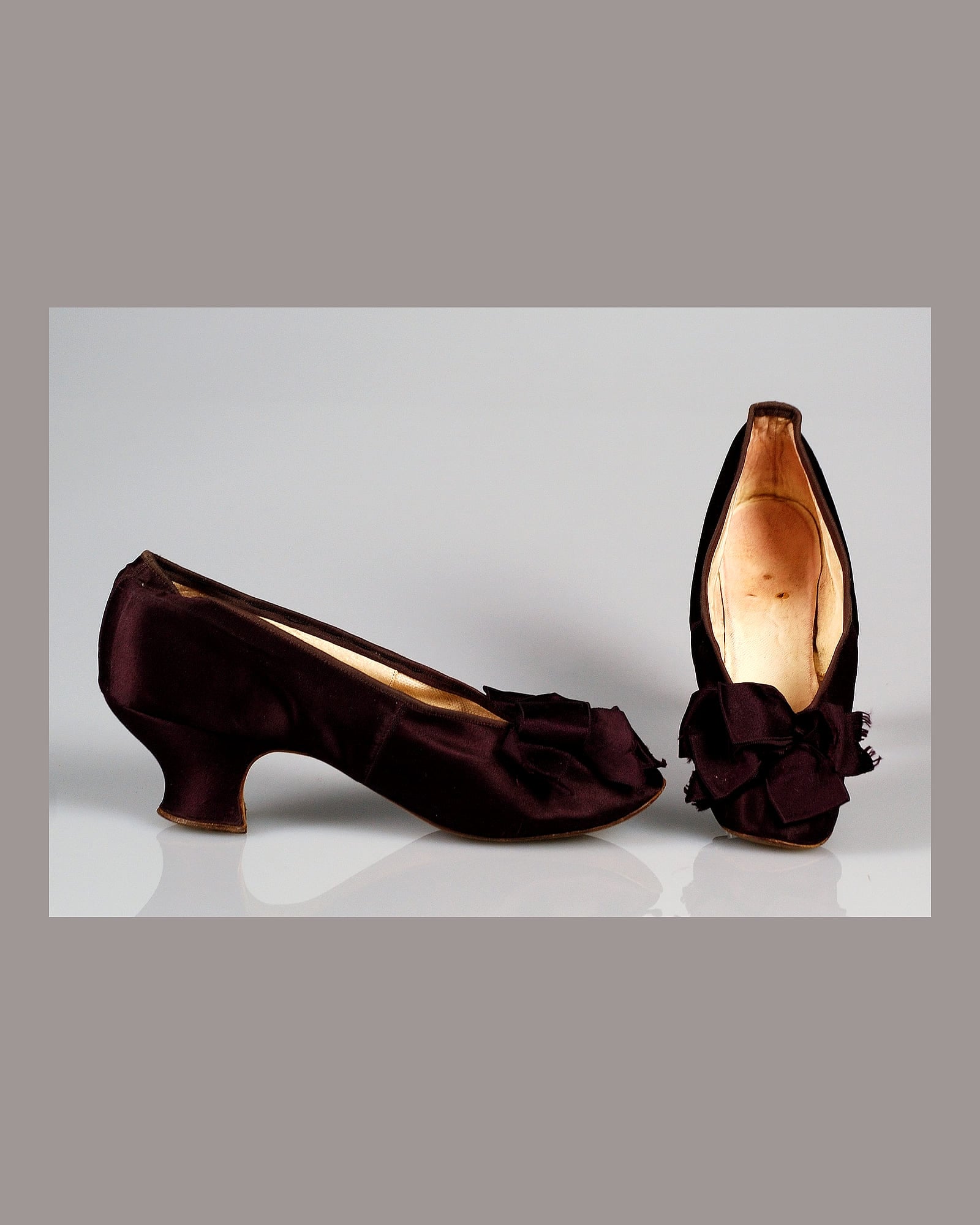 Pair of burgundy silk heels with ribbon bows, grey background