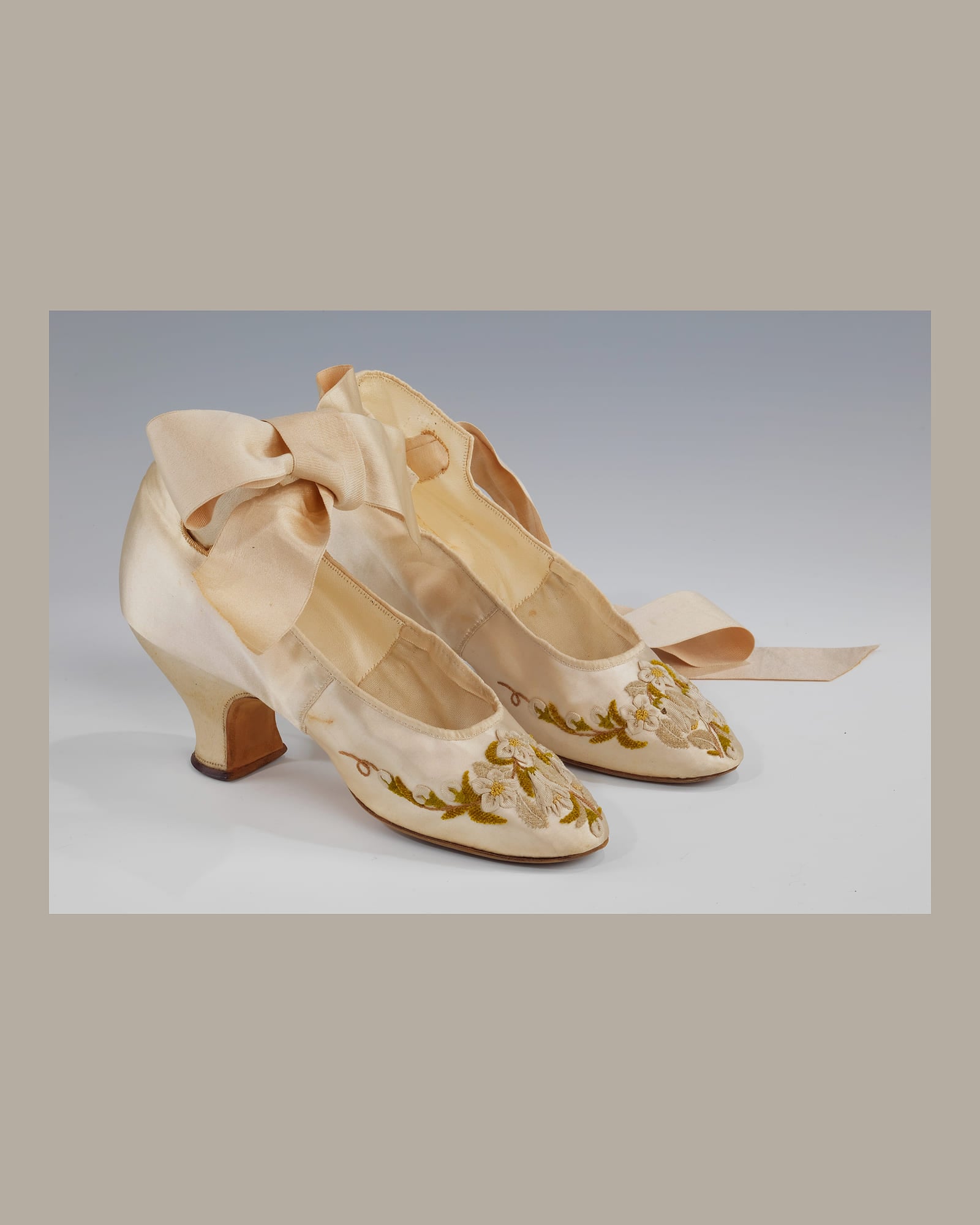 Pair of ivory satin slippers with ribbon ties, grey background