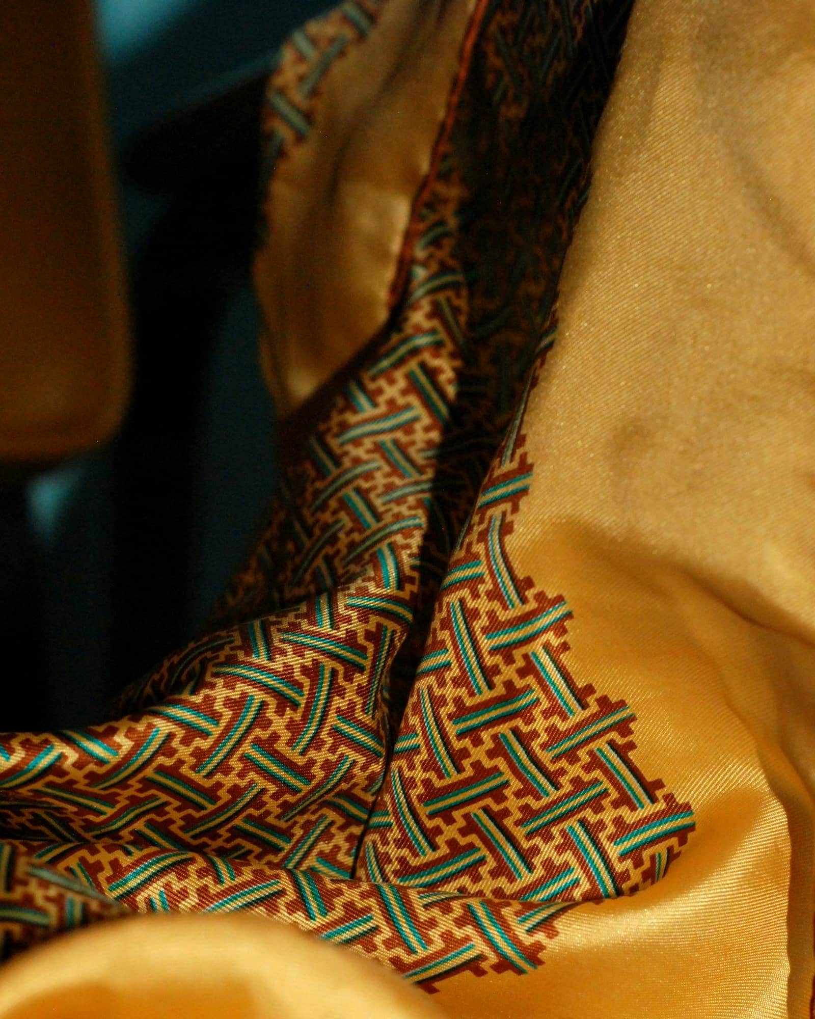 Ochre silk scarf with a green geometric border, folded across a chair