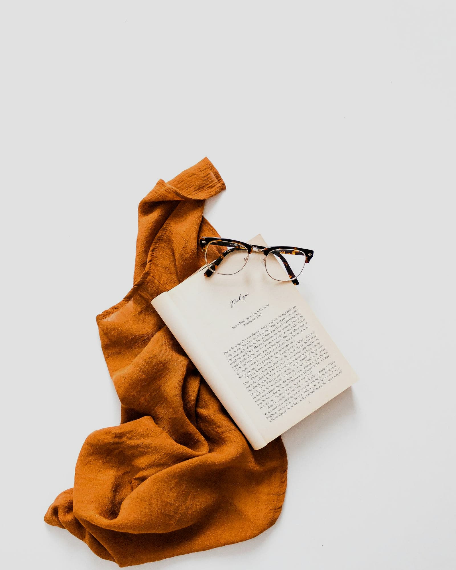 Rust-coloured scarf pooled on a white surface beside an open book